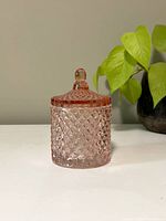 Front view of vintage pink glass container with lid on, showing the diamond pattern texture and small knob on top.
