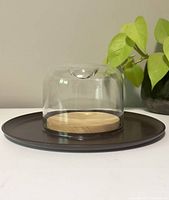 Showing entire setup of vintage Pyrex cheese plate with clear glass dome cover on dark base with wooden insert.