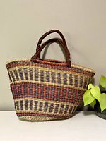 Front view of vintage wicker market bag showing multi-color woven pattern with black, red, and natural fibers and leather handles.