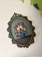 Front view of vintage oval shaped flower portrait in wood and brass frame, showing floral arrangement with blue vase.
