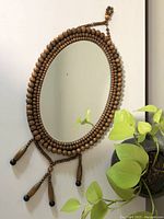 Front view of the oval mirror hanging with the wooden bead frame and tassels clearly visible