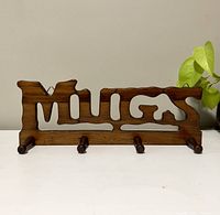 Front view of the wooden mug rack showing the word 'MUGS' cutout and 4 pegs.