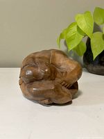 Front angle view of the wooden weeping Buddha statue showing the top of the head and folded arms.