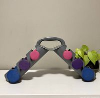 Front view of gray plastic rack holding six neoprene hand weights, three pairs in pink, purple, blue.