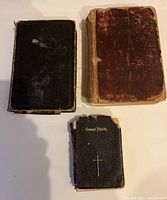 Three antique books on a surface: New Testament in Greek, Book of Common Prayer, and Pearl Bible