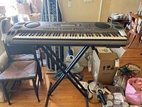 Front view of the Casio WK-1300 electronic keyboard on black X-style stand in room with wooden floor and packaging boxes nearby.