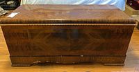 Front view of vintage wooden cedar chest showing wood veneer finish, scratches, and wood chipping on bottom edge.