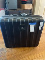 Front view of black DJI Inspire hard case with scratches, showing DJI logo and model area.