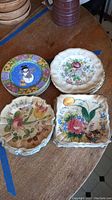 Eight plates grouped by style: colorful hand-painted Italian plates with floral and fruit motifs and Sango blue plates with chef design.