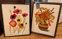Two framed needlepoint floral art pieces side by side with visible details of the flowers and frames