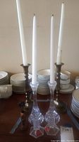 Two Towle full lead crystal candle holders with hexagonal bases flanked by two bronze candlestick holders, each holding a white taper candle