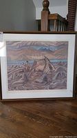 Front view of framed and matted print depicting rocky landscape with figures, tent, mountains, and clouds.
