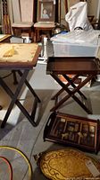Overview of folding tray table with crossed legs and multiple serving trays stacked below and beside it, showing basement setting.