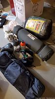 Photo showing multiple camping items spread on floor including North 49 mat, sleeping bag, lantern, stove, cups, and bug jacket bags.