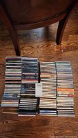Two boxes full of stacked music CDs on a wooden floor arranged upright with spine labels visible.