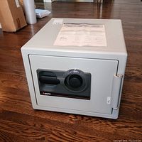 Front and side view of the light gray Sentry fire safe model S0209 with combination dial lock and handle, sitting on wooden floor.