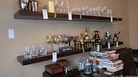 Photo of two dark wood floating shelves installed on wall, holding glassware and decorative items.