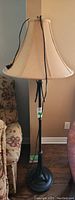 Full view of the floor lamp showing the beige fabric shade and dark metal base near upholstered furniture.