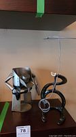 Photo showing both metal cowboy sculpture and cowboy with lasso wine bottle holder on a dark wood surface.