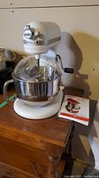 Front view of white KitchenAid bowl-lift stand mixer with stainless steel mixing bowl and instruction manual