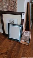 Collection of large, medium, and small new picture frames in different colors and finishes stacked and leaning against a wall.