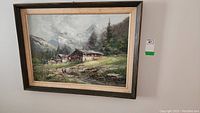 Frontal view of the framed oil painting depicting a cabin in a mountainous landscape with greenery and pine trees.