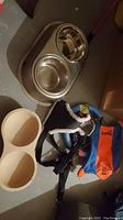 Photo of stainless steel double bowls in metal stand, beige double plastic bowl, black pet harness with leash, orange blue and yellow toys on floor