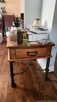 Front and side view of the wooden side table with various items on top, showing the drawer and metal legs.