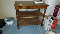 Wooden table with two lower shelves seen from front, surrounded by miscellaneous basement items.