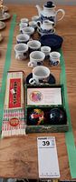 Full view of six person tea set including teapot, cups, saucers, creamer, sugar bowl, chopsticks and exercise balls on wooden table.