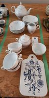 Porcelain tea set arranged on table including teapot, six dessert plates, six small bowls, sugar bowl, creamer, six teacups and saucers.