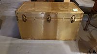 Front view of vintage metal steamer trunk showing three metal latch locks and gold-tone finish