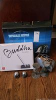 Photo of the boxed Waterfall picture, Buddha Board set, two metallic spherical objects, glass candle holders with candles, and a small container with decorative natural items on the floor.