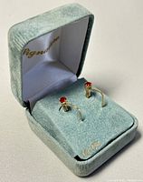 Pair of 10K gold earrings with red garnet stones displayed in a blue velvet box with marking on pillow.