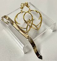 Gold-toned drop earrings and silver gold-toned bracelet displayed on clear stand showing entire set.