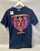 Front view of black Journey Greatest Hits t-shirt with colorful winged emblem graphic and text.