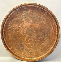 Full view of the large round copper tray showing etched and hammered decorative patterns with a raised rim and signs of age-related corrosion.