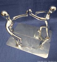 Full view of one stainless steel figural bookend showing the abstract figure and rectangular base on dark blue fabric background.