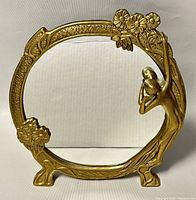 Front view of the brass vanity mirror showing embossed floral border and bas-relief woman holding child figure.
