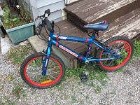 Full view of child's bike showing side profile with blue and red frame and red rims.
