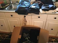 Folded blue denim jeans and other dark colored clothing items laid on counter, with cardboard box below containing more clothes.
