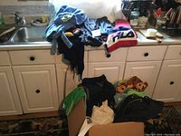 Lot of boys size 4-5 clothing including tops, hooded towels, and karate outfit displayed on kitchen counter and chair.