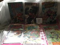 Collection of seven vintage comic books in clear protective sleeves, titles visible include Flash, Hulk, Justice League, and Marvel Comics.