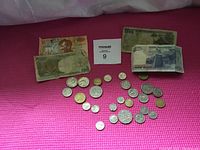Overview of used banknotes and assortment of coins laid out on a pink surface.