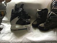 Photo showing one pair of black and white ice skates with laces and plastic blade holders and one pair of black Kodak hiking boots with laces and rugged soles, placed on a white cloth.