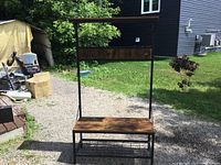 Full view of standing coat rack with bench and wooden board with hooks at top, metal frame.