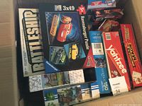 Photo showing Ravensburger Disney Pixar Cars puzzle, Battleship game, Yahtzee, and other boxed games piled in a box