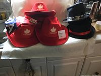 Photo showing the full collection of holiday hats including three red Canada hats, one Canada hat with Canadian flag, and two New Year black hats with bands.