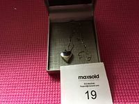 Photo of silver heart-shaped locket necklace in gray jewelry box on pink background, showing pendant and chain details.