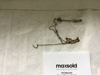 Photo showing the entire gold chain with the 'Texas' script pendant placed on a white fabric background along with a Maxsold card.